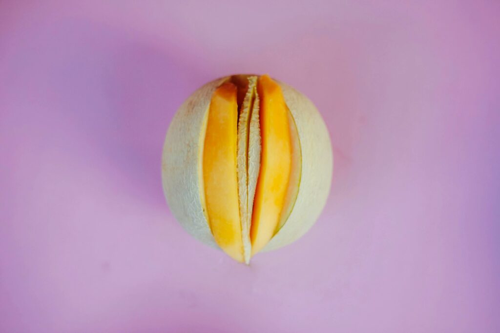 Top view of a sliced melon on a bold pink surface, showcasing contrast and freshness.
