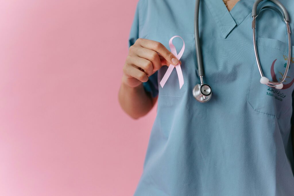 Healthcare worker in scrubs holds a pink breast cancer awareness ribbon symbolizing support.