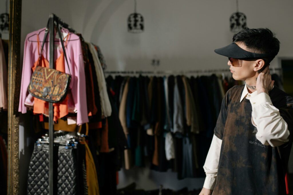 Man wearing sunglasses and sun visor browsing clothes rack at thrift store.